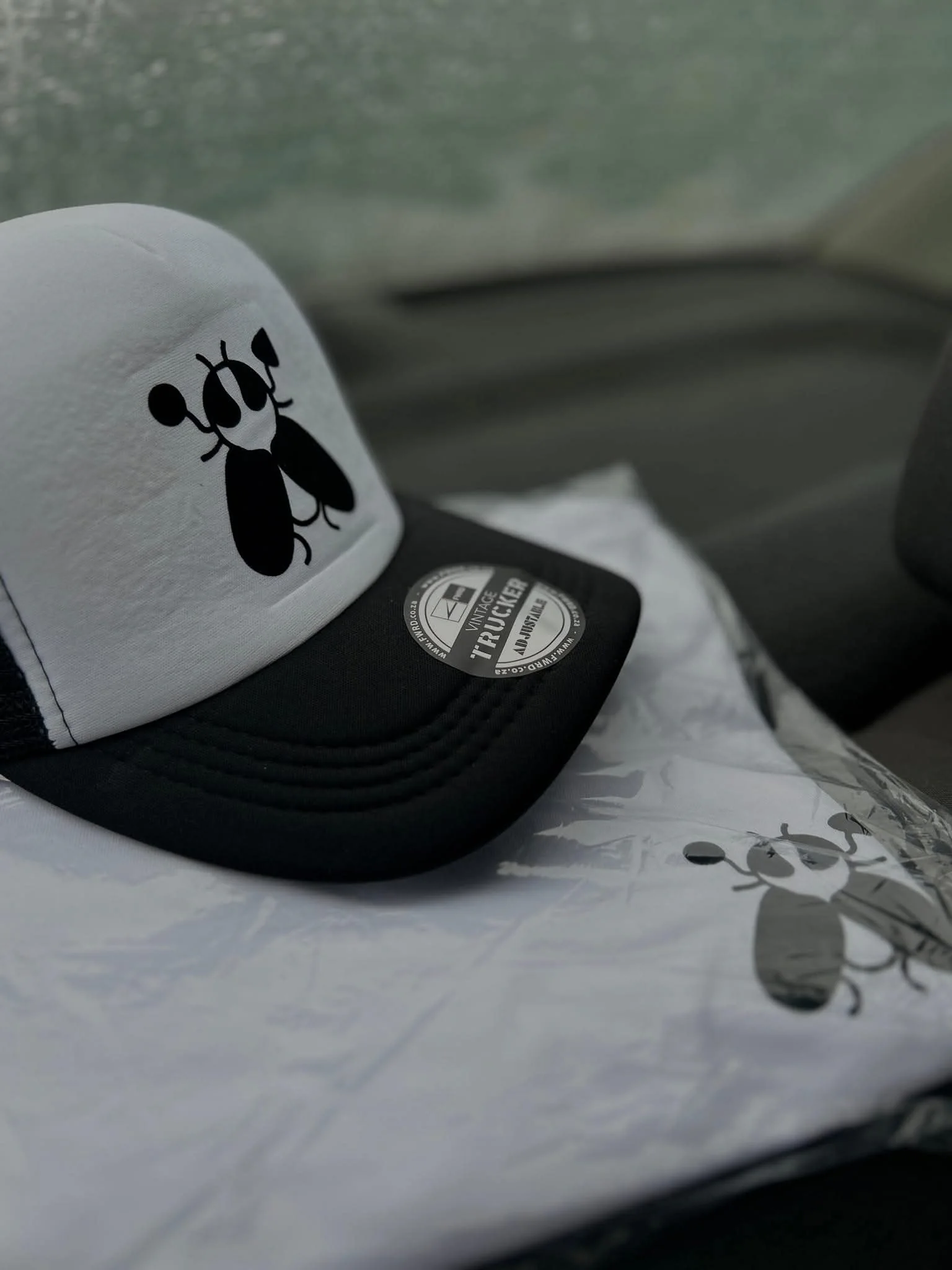 A grey and black SACXESS trucker cap with the beetle mark, resting on a folded garment